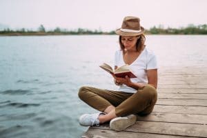 woman reading a book on a deck near the lake