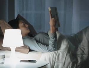 woman reading book in bed with lamp on