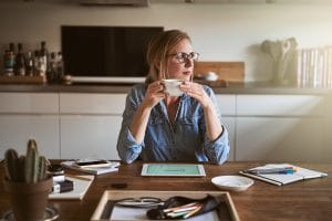 Woman reflecting at her kitchen table drinking coffee