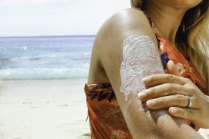 woman putting sunscreen on her arm at the beach