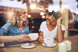 two multi ethnic friends having drinking coffee and smiling during a conversation