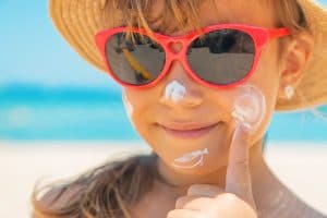 Young girl with red sunglasses on putting sunscreen on her face