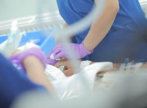 critical care nurse in blue scrubs assisting patient in their bed
