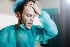 male nurse in surgical scrubs with hand on his head in distress