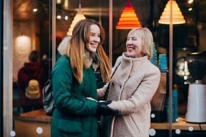 adult daughter and older mother embracing and smiling outside of a store