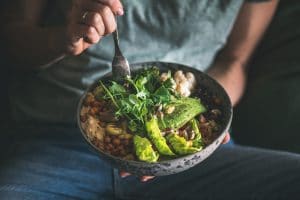 woman in t-shirt and jeans eating a buddha bowl