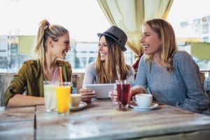 3 woman laughing and chatting over lunch at a restaurant