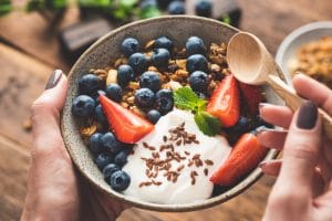 upclose of a woman holding a bowl of fruit and yogurt with her spoon in hand