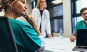 nurse sitting at conference room table with other medical professionals thinking about issue.