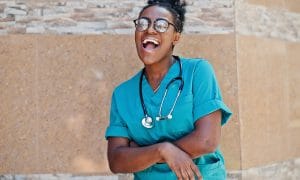 Black nurse wearing glasses and laughing outside