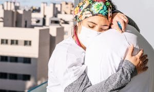 two nurses hugging each other outside with masks on.