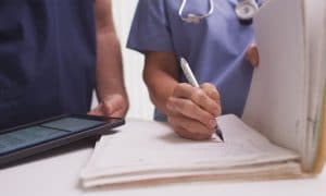 nurse reviewing paper chart with a pen.