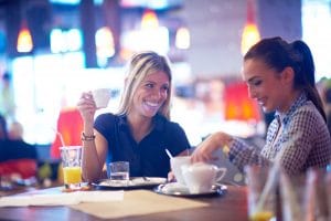 two young women drinking coffee and smiling at a cafe